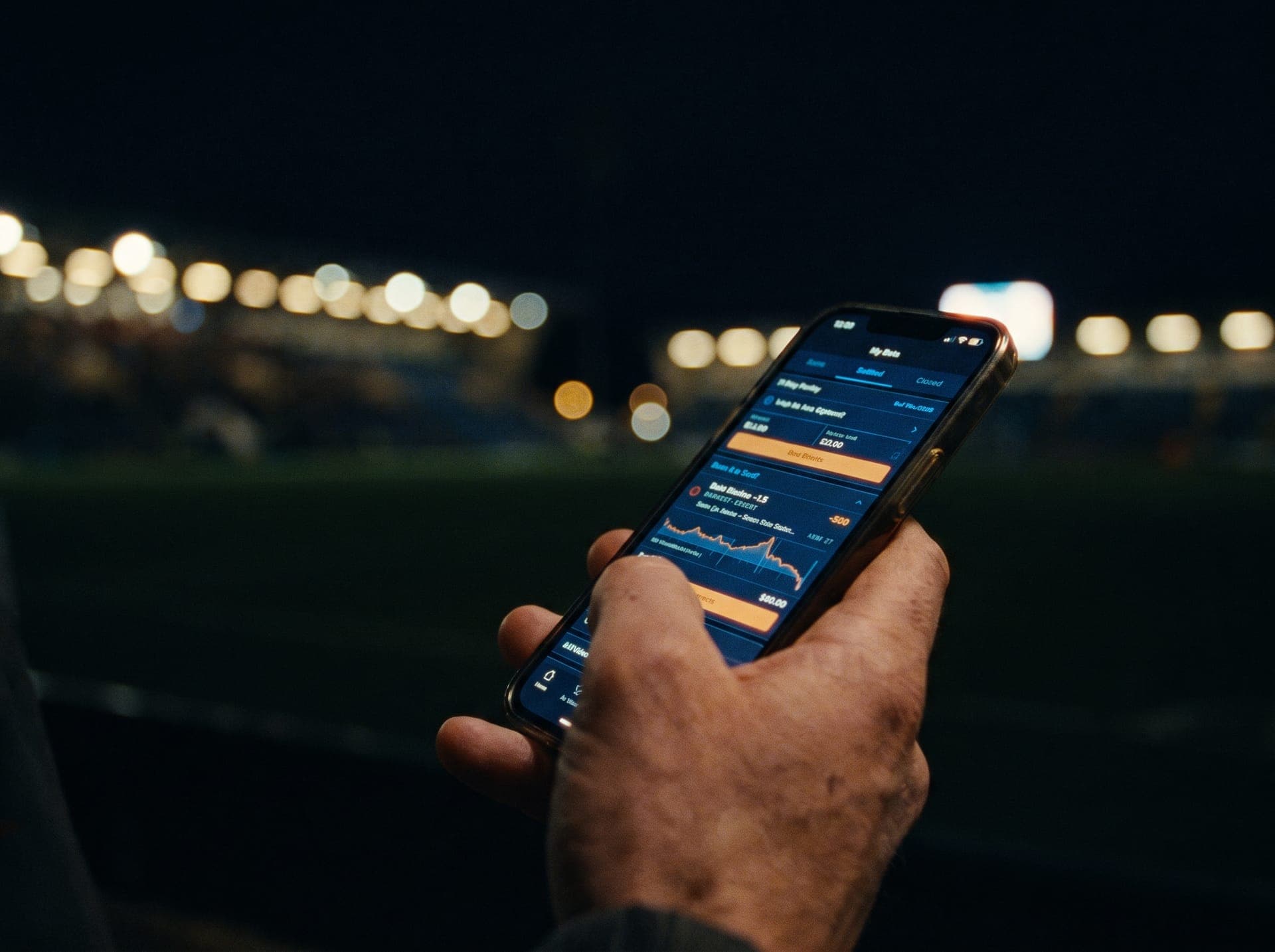 Hand holding a phone with a glowing betting slip at night
